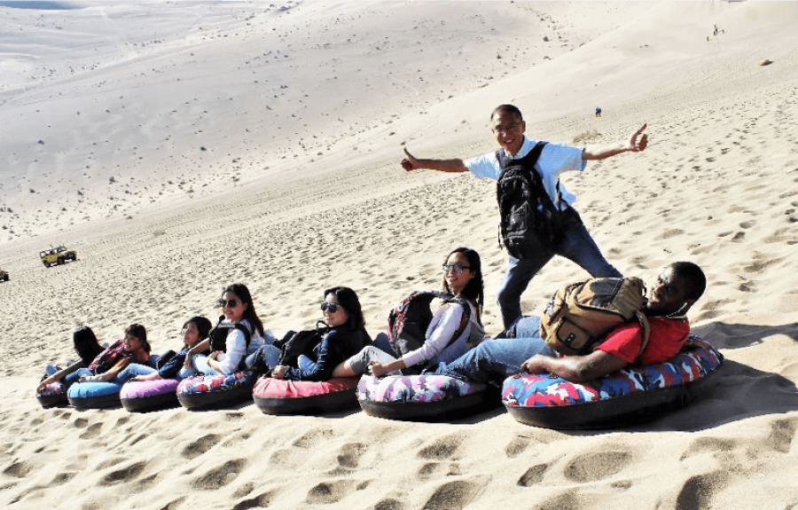 People riding sleds on a sand dune